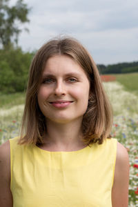 A beautiful young blonde woman in a yellow dress stands among a flowering field