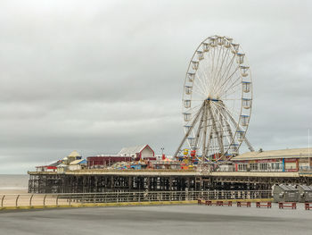 Ferris wheel at amusement park against cloudy sky