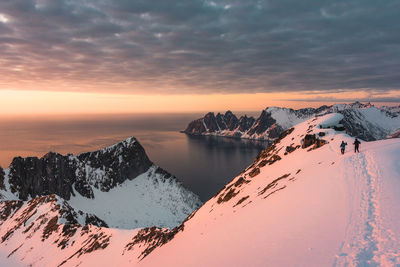 Scenic view of snowcapped mountains by sea against cloudy sky during sunset