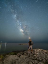 Rear view of man standing on mountain against sky at night