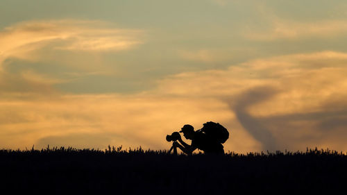 Silhouette couple on field against sky during sunset