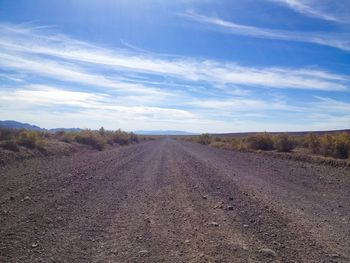 Dirt road amidst field against sky