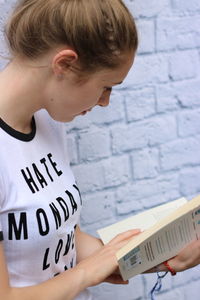 Girl reading book against brick wall