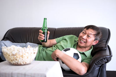 Mature man watching sport while lying on sofa at home