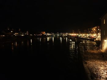 Illuminated buildings by river against sky at night