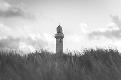 Lighthouse on field by building against sky