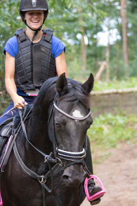 Smiling woman riding horse on field at forest