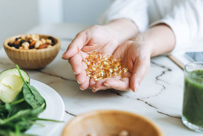 Woman doctor nutritionist hands in white with omega 3, vitamin d capsules with green vegan food