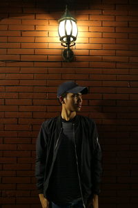 Young man standing against illuminated brick wall at night