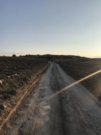 Empty road amidst field against clear sky