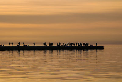 Silhouette people on sea against sky during sunset