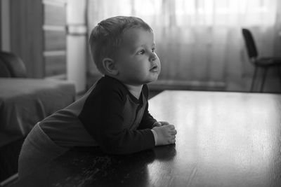 Cute baby boy looking away while standing by table at home