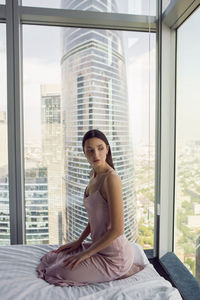 Woman in a nightgown sit on the bed window in a skyscraper near the bed