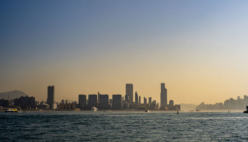 Sea by buildings against sky during sunset