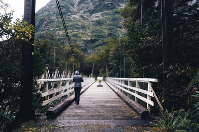 Rear view of person walking on footbridge leading towards mountain