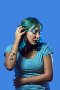 Young woman looking away while standing against blue background