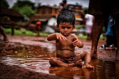 Full length of shirtless boy playing on mud