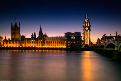 Illuminated buildings by river against sky in city at night