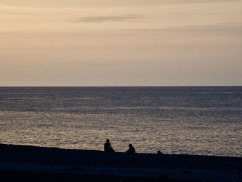 Silhouette people on sea against sky during sunset