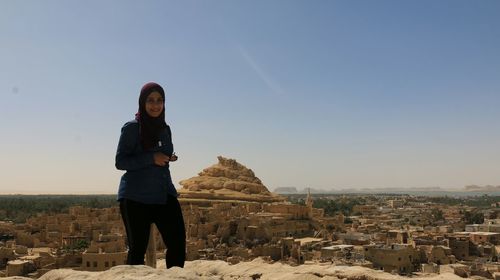 Portrait of smiling young woman standing against clear sky