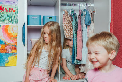 Children, sisters, girlfriends, twins play, laugh, have fun, hide at home in the closet with clothes
