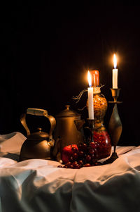 Close-up of lit candles with teapots on table against black background