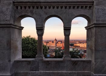 Hungarian parliament building in city during sunset seen through arch