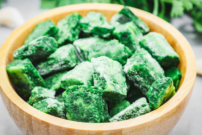 Frozen spinach cubes in a wooden bowl lie on a light gray cement.