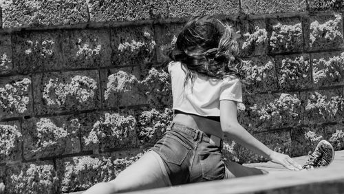 Rear view of woman sitting on retaining wall