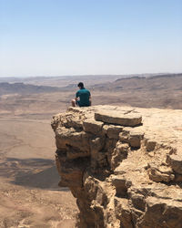 Rear view of man sitting on rock