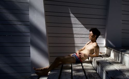 Full length of shirtless young man laying on wall stair in swimsuit