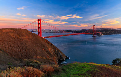 Suspension bridge over sea against sky during sunset