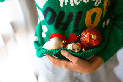 Midsection of woman carrying christmas ornament in sweater