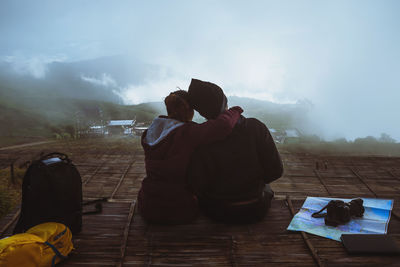 Rear view of couple sitting on mountain against sky