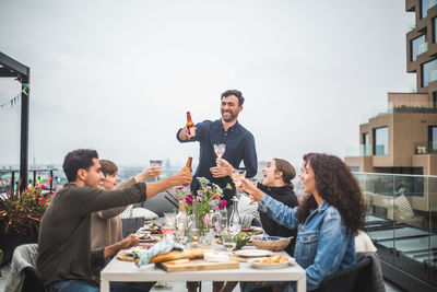 Young male toasting drinks with friends during social gathering on rooftop