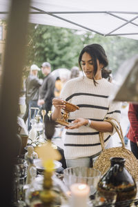 Young woman buying antique standing near stall while doing shopping at flea market