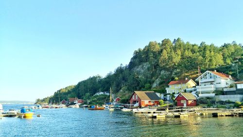 Houses by river and buildings against clear sky