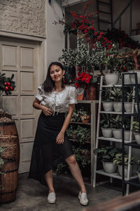 Portrait of smiling young woman standing by potted plants