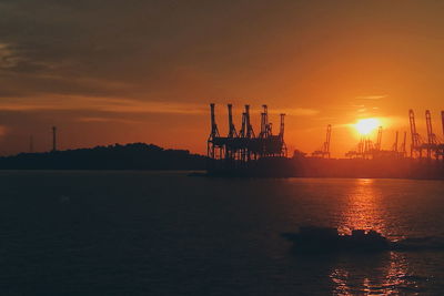 Silhouette cranes by sea against sky during sunset