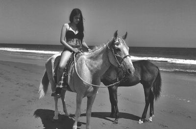 Young woman sitting on horse against sky at beach