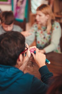 Rear view of young man decorating easter eggs while sitting on table indoors