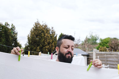 Man with clothespin drying sheets at back yard