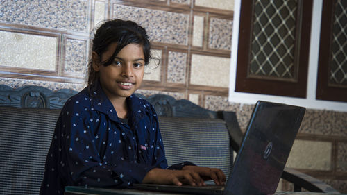 Portrait of a smiling young woman using phone while sitting on table