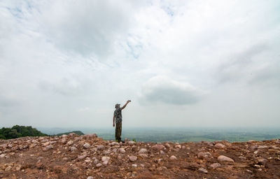 Man standing on rock by sea against sky