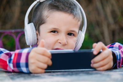 Cute boy listening music while using mobile phone outdoors