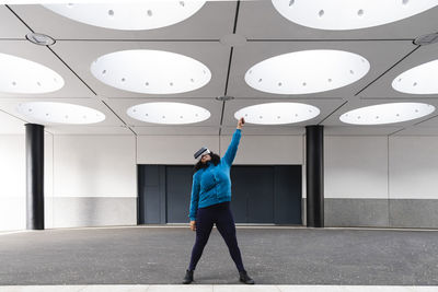 Woman raising hand wearing vr headset under illuminated ceiling