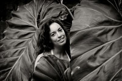 Portrait of young woman hidden between some giant tropical leaves 