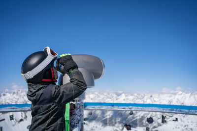 A boy in ski helmet looks through a telescope at the mountains in austria, tirol