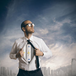 Young man with arms outstretched standing against sky