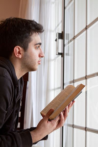 Side view of young man looking through window